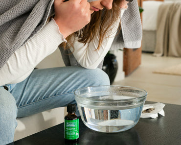 Person wrapped in a blanket with a bowl of water and a eucalyptus bottle on a table