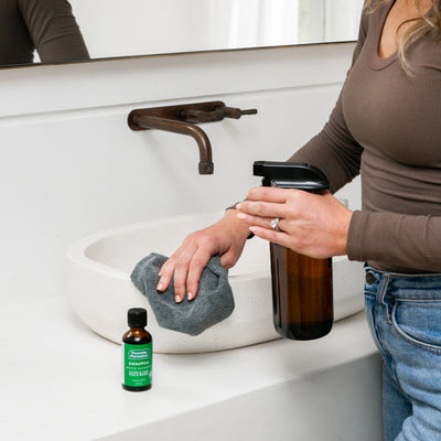 Person washing hands with a bottle eucalyptus oil and a cloth in a bathroom.