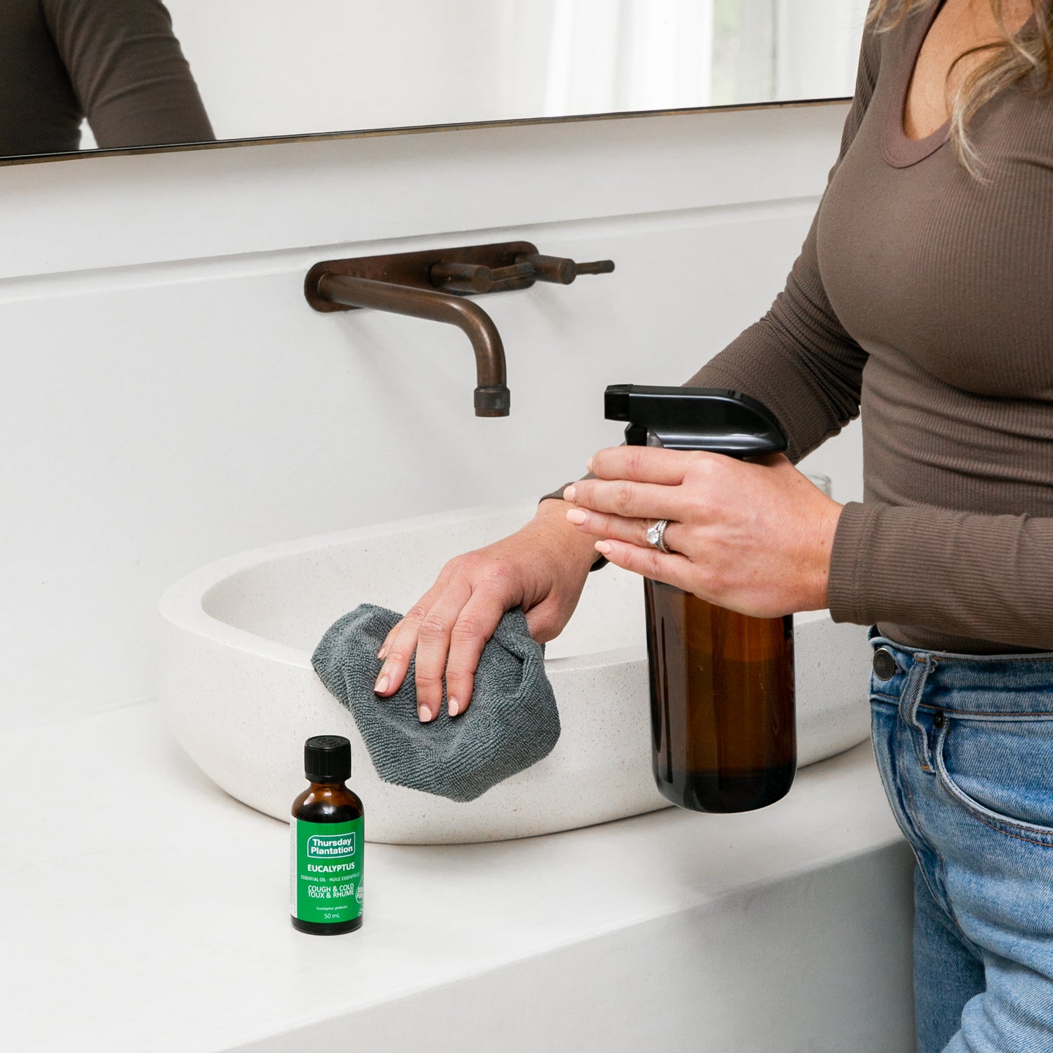 Person washing hands with a bottle eucalyptus oil and a cloth in a bathroom.