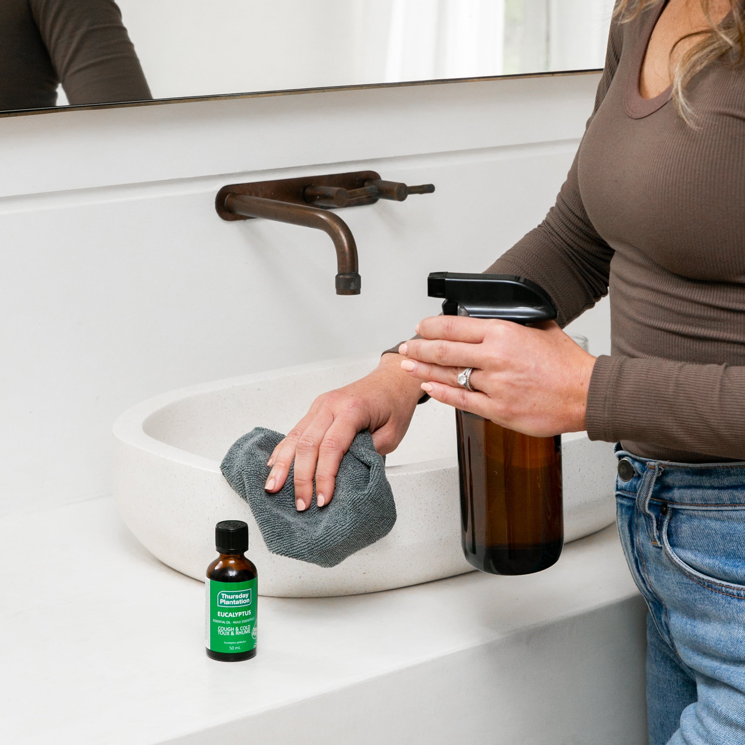 Person washing hands with a bottle eucalyptus oil and a cloth in a bathroom.